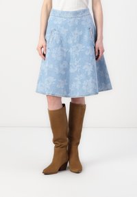 Light blue floral-patterned denim skirt with a flared design, featuring side pockets and a soft texture, paired with brown knee-high boots.