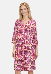 Blumenkleid mit V-Ausschnitt, dreiviertellangen Ärmeln und knielanger Schnittform. Das Design zeigt lila und rosa Blumen auf einem hellen Hintergrund.