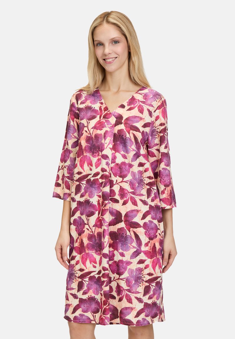 Blumenkleid mit V-Ausschnitt, dreiviertellangen Ärmeln und knielanger Schnittform. Das Design zeigt lila und rosa Blumen auf einem hellen Hintergrund.