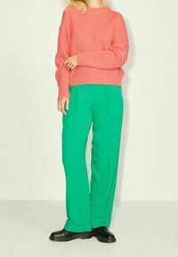 Pull rose côtelé à manches longues associé à un pantalon vert à jambes larges, avec une texture lisse et des bottes noires épaisses.