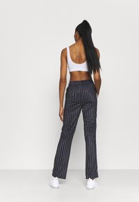 Marineblaue, gestreifte Hosen mit lockerem Sitz, elastischem Bund und leichtem Stoff. Kombiniert mit einem weißen, kurz geschnittenen Oberteil und weißen Sneakern.