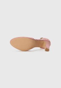 Chaussure à talon haut en suède rose avec un bout arrondi et un petit détail de boucle en or sur le côté. Tige lisse et texturée, semelle en caoutchouc beige.
