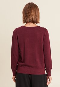 Bordeaux gebreide trui met lange mouwen, ronde halslijn, geribde manchetten en tailleband, met een gladde textuur en minimale naden.