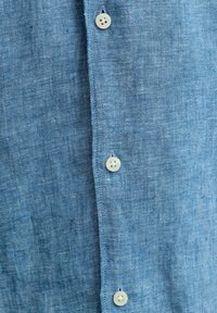 Primer plano de tela texturizada azul con tres botones blancos y ojales en una fila vertical.