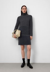 Grijze gebreide coltrui met een fuzzy textuur, gecombineerd met een bijpassende rok. Accessoires zijn een kleine beige schoudertas en zwarte schoenen.
