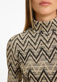 Hochkragenoberteil aus strukturiertem Stoff mit zigzagförmigem Muster in Schwarz und Beige. Eng anliegendes Design mit geripptem Saum.