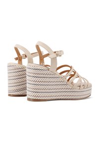 Sandali con zeppa beige, dotati di cinturini incrociati in ecopelle e una piattaforma intrecciata accentuata. Chiusura con fibbia alla caviglia per una vestibilità sicura.
