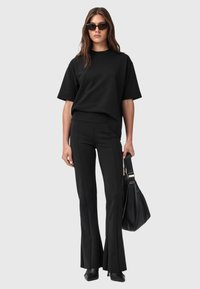 Zwarte oversized t-shirt met korte mouwen, gecombineerd met aansluitende zwarte flared broek. Accessoires omvatten een grote zwarte handtas en donkere zonnebril.