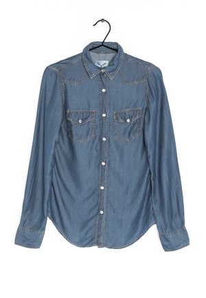 Džínová košile světle modré barvy s předním zapínáním na knoflíky, špičatým límečkem, dvěma kapsami na prsou a zaobleným spodním okrajem. Celá košile je zdobena kontrastními stehy.