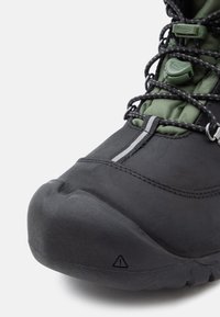 Crne vodootporne planinarske čizme s teksturiranim gumiranim vrhom, zelenim podstavom i sustavom brzog vezanja za sigurno prianjanje. Imaju reflektirajući detalj.