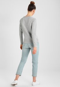 Grå långärmad sweatshirt med rund halsringning, kombinerad med ljusblå slitna jeans och vita sneakers, sedd bakifrån.