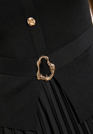 Must mustritsiga seelik koos sobiva kootud topiga, millel on kuldne ebaühtlase kujuga vöö pandla ja kuldse nööbi detail.