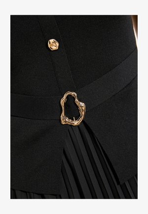 Must mustritsiga seelik koos sobiva kootud topiga, millel on kuldne ebaühtlase kujuga vöö pandla ja kuldse nööbi detail.