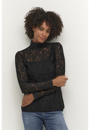 Black lace long-sleeve top with a high neckline and scalloped edges, featuring floral patterns and a fitted design, paired with blue jeans.