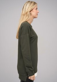 Sweatshirt vert olive à manches longues, col rond et poignets côtelés. Présente un détail zip à l'ourlet. Tissu doux et décontracté.