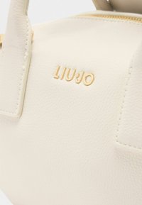 Borsa a tracolla beige con texture e hardware dorato, con il nome del marchio "LIU JO" impresso nella parte anteriore. Design compatto con manici corti.