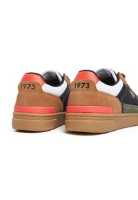 Zapatillas en marrón y azul marino con parte superior de ante y malla, acentos naranjas en el talón y el número "1973" impreso en la parte trasera. Suela de goma.