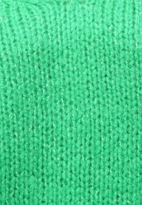 Πράσινος πλεκτός ύφασμα με υφή και σχέδιο, που παρουσιάζει μια μαλακή, φουντωτή εμφάνιση και μικρές παραλλαγές στο χρώμα σε ολόκληρη την επιφάνεια.