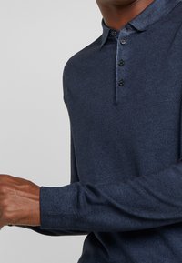 Navyblaue Langarm-Polohemd aus strukturiertem Strick, mit einer Knopfleiste mit drei Knöpfen und feinen Kragenakzenten.