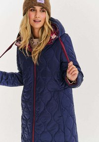 Granatowy pikowany płaszcz z kapturem, z bordowymi akcentami i kwiatową podszewką. Wykonany z gładkiego, lekkiego materiału.