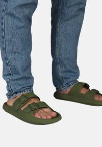 Sandales en caoutchouc vertes avec deux boucles réglables, semelle plate et design ouvert, assorties à un jean en denim bleu clair.