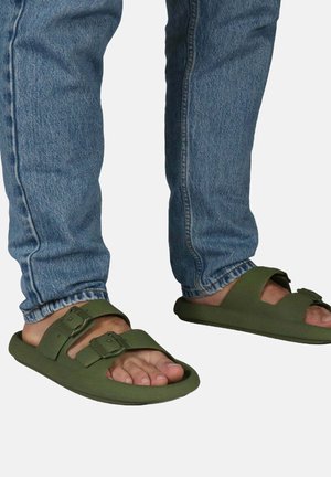 Sandales en caoutchouc vertes avec deux boucles réglables, semelle plate et design ouvert, assorties à un jean en denim bleu clair.