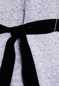 Tissu gris à la finition texturée avec une ceinture en velours noir. La ceinture est nouée au centre, mettant en valeur la silhouette du vêtement.