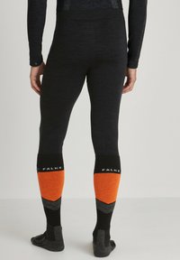 Leggings térmicas negras con calcetines de esquí de patrón naranja y gris. Los calcetines tienen una parte superior negra y diseños contrastantes en naranja y gris.