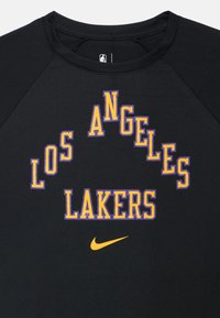 Czarny t-shirt z napisem "LOS ANGELES LAKERS" w łuku, w kolorach fioletowym i żółtym, z logo Nike w kolorze pomarańczowym. Gładka tkanina, okrągły dekolt.