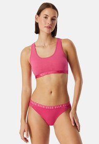 Vaaleanpunainen puuvillainen urheiluliivit leveillä olkaimilla ja joustavalla helmalla. Vastaavat vaaleanpunaiset bikinihousut, joissa on logovöinen vyötärö ja sileä pinta.