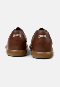 Adidași din piele maro cu o formă rotundă, talpă din cauciuc moale și sigla "CAMPPER" pe toc, scrisă cu text alb.