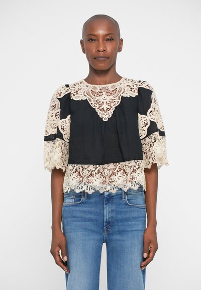 Schwarze Bluse mit beigen Spitzenakzenten, rundem Ausschnitt, kurzen Ärmeln und einem aufwändigen Spitzenabschluß am Saum.