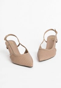 Beige korkkilappuiset slingback-kengät, joissa on kudottu pinta, lyhyet korot ja säädettävä nilkkaremmi. Sileä sisustus logotyyppisellä yksityiskohdalla.