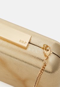 Cartera de mano dorada con textura de cuero agrietado, herrajes en tono dorado y una cadena como asa. Presenta un cierre de metal brillante con detalle de marca.