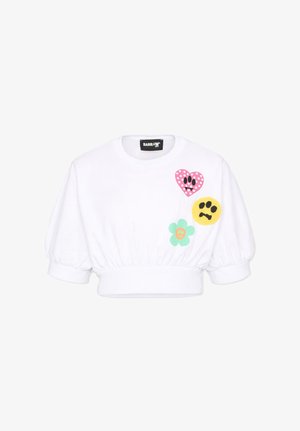 Sweat-shirt blanc court avec manches bouffantes, orné de patches en forme de cœur à pois roses, visage triste jaune et fleur verte sur la poitrine.