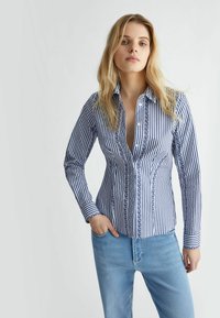 Camicia a righe blu e bianche con colletto button-down e rifiniture decorative lungo il davanti. Maniche lunghe con polsini abbottonati. Tessuto di cotone.
