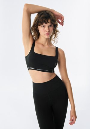 Black sports bralette with a square neckline and thick straps. Features white accent lines. Worn with high-waisted black leggings.