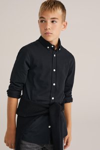 Melna garām piedurknēm krekls ar baltām pogām, strukturēta auduma, un klasisku apkakli; apvienots ar strukturētu melnu džemperi, kas sasietas ap vidukli.