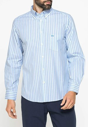 Uomo che indossa una camicia a righe verticali azzurro chiaro e bianco con maniche lunghe e pantaloni blu scuro.