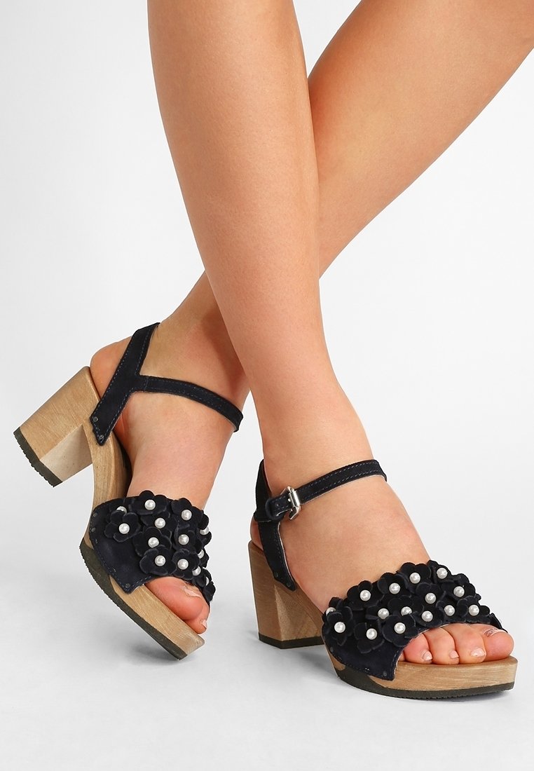 Sandali con tacco in suede nero con accenti floreali e dettagli in perle sulle cinghie. I tacchi a blocco in legno offrono stabilità e altezza.