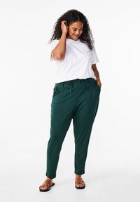Green tapered pants with an elastic waistband and drawstring, paired with a white t-shirt. The fabric appears smooth, with a relaxed fit.
