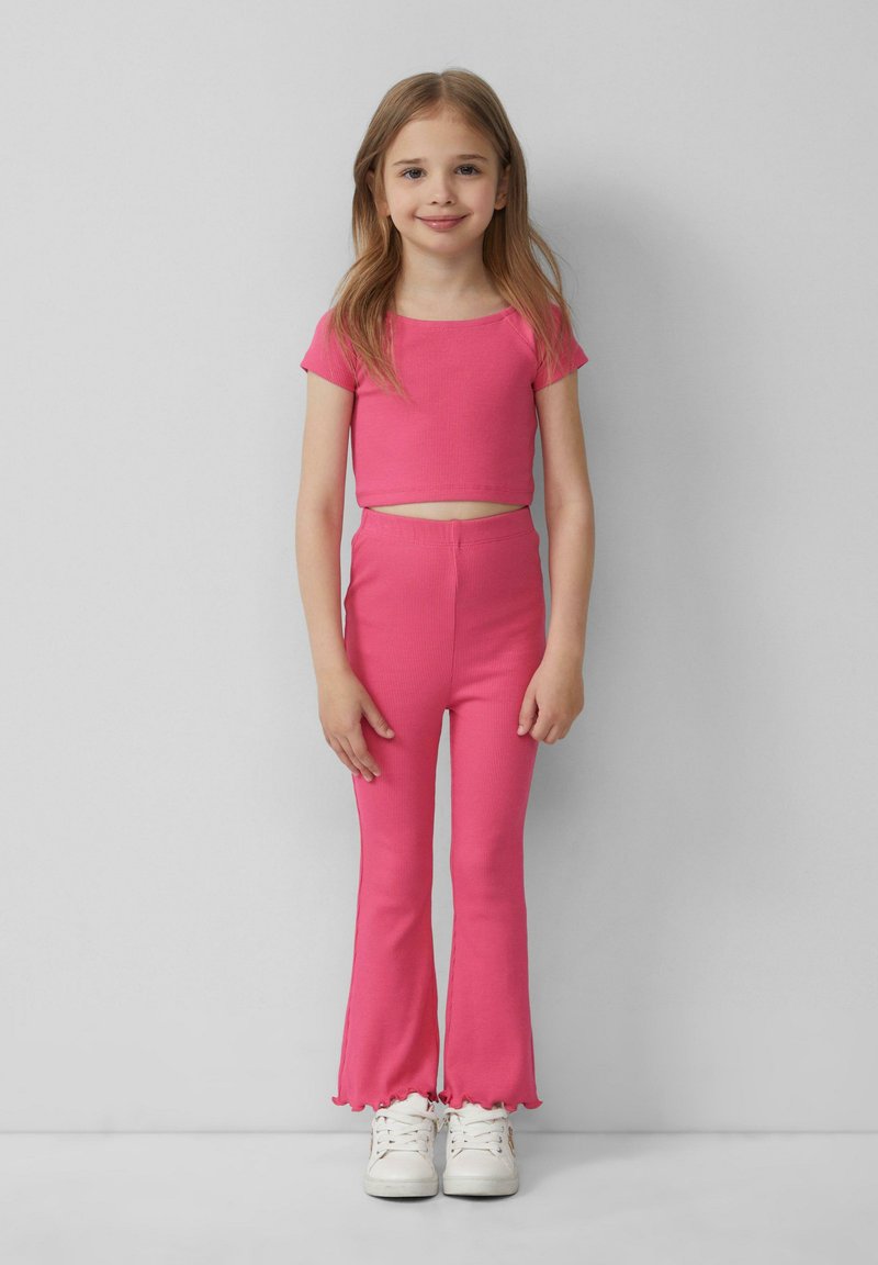 Roze geribbelde crop top en bijpassende flared leggings met een geschulpte zoom. Gepaard met witte sneakers.