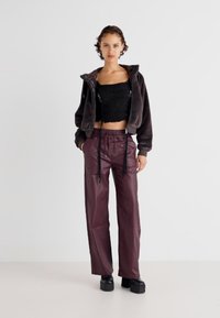 Črn pleten top, siva puhasta zip-up jopica, burgundska usnjena široka hlače, in masivne črne platforme.