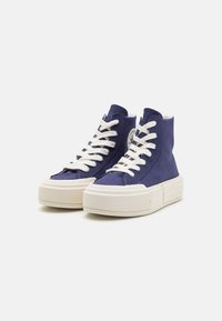 High-top sneakers in navy canvas with white laces. Features a thick cream-colored sole and a circular logo detail on the side.