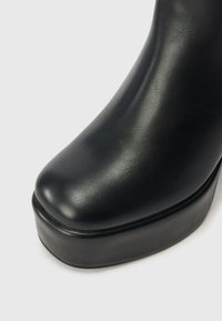 Botín de tobillo de imitación cuero negro con puntera redonda y suela de plataforma. Textura suave, ligero brillo y diseño aerodinámico.