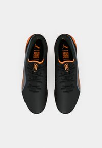 Scarpe sportive nere con accenti arancioni, design elegante, superfici testurizzate e un codice QR sulle sole interne. Presentano lacci e pannelli in rete laterali.