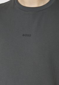 Tmavě šedé bavlněné tričko s kulatým výstřihem a jemným, tón v tónu emblémem "BOSS" na hrudi. Hladká textura, ležérní střih.