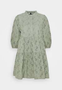 Ljust grön lager-på-lager klänning med blommigt hålmönster, rund krage och puffärmar, tillverkad av strukturerad tyg.