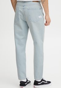 Jeans de denim azul claro con un diseño de pierna recta, que cuentan con dos bolsillos traseros y una etiqueta de marca en la cinturilla.