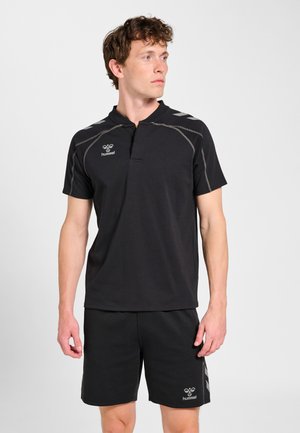 Mand iført sort sports-T-shirt med korte ærmer og matchende shorts med grå syninger og Hummel-logoer, stående mod en ensfarvet hvid baggrund.